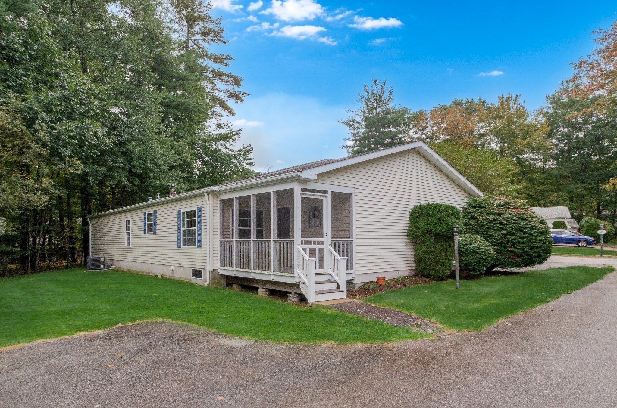 Light-sided home with a screened front porch and lawn among mature trees.