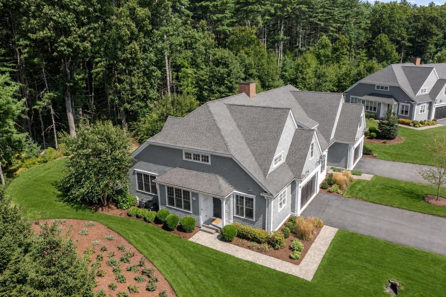 Aerial view of gray homes with landscaped lawns beside dense woodland.
