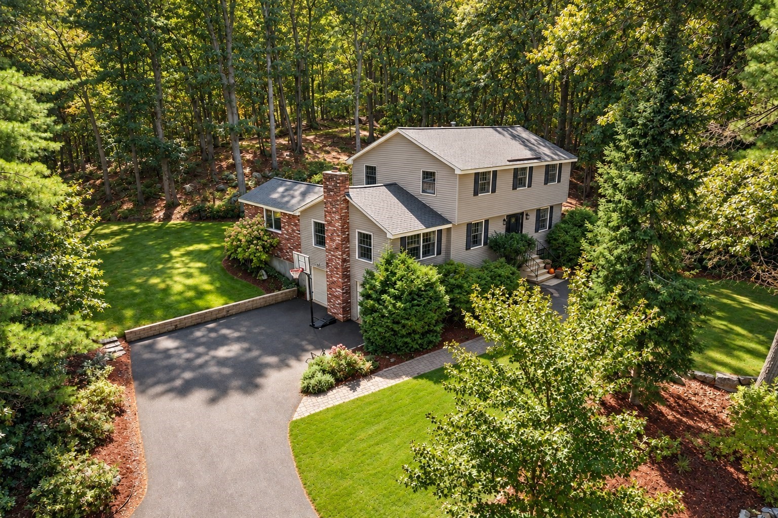 Aerial view of a beige two-story house with a brick chimney, landscaped lawn, and curving driveway.