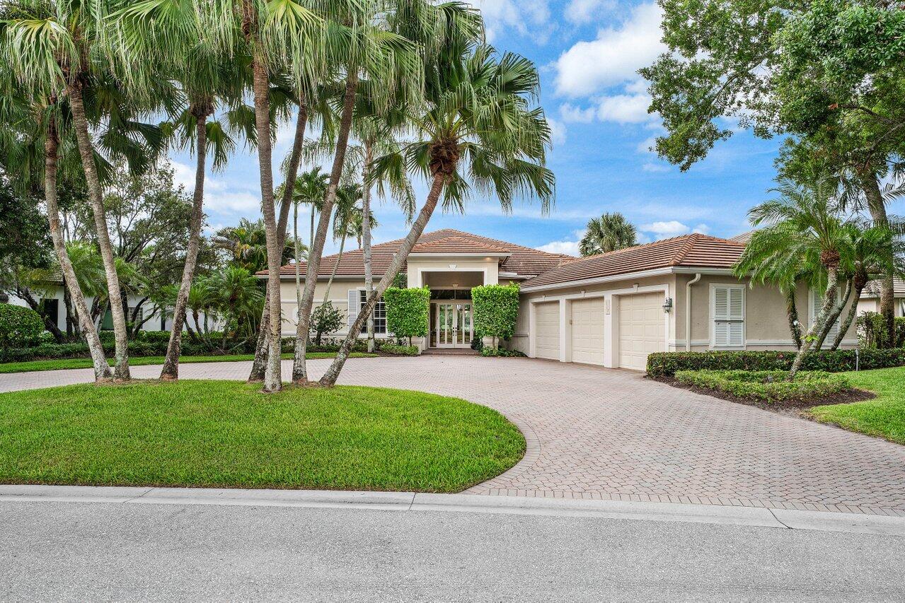 Single-story home with a three-car garage, curved paver driveway, and tall palms.