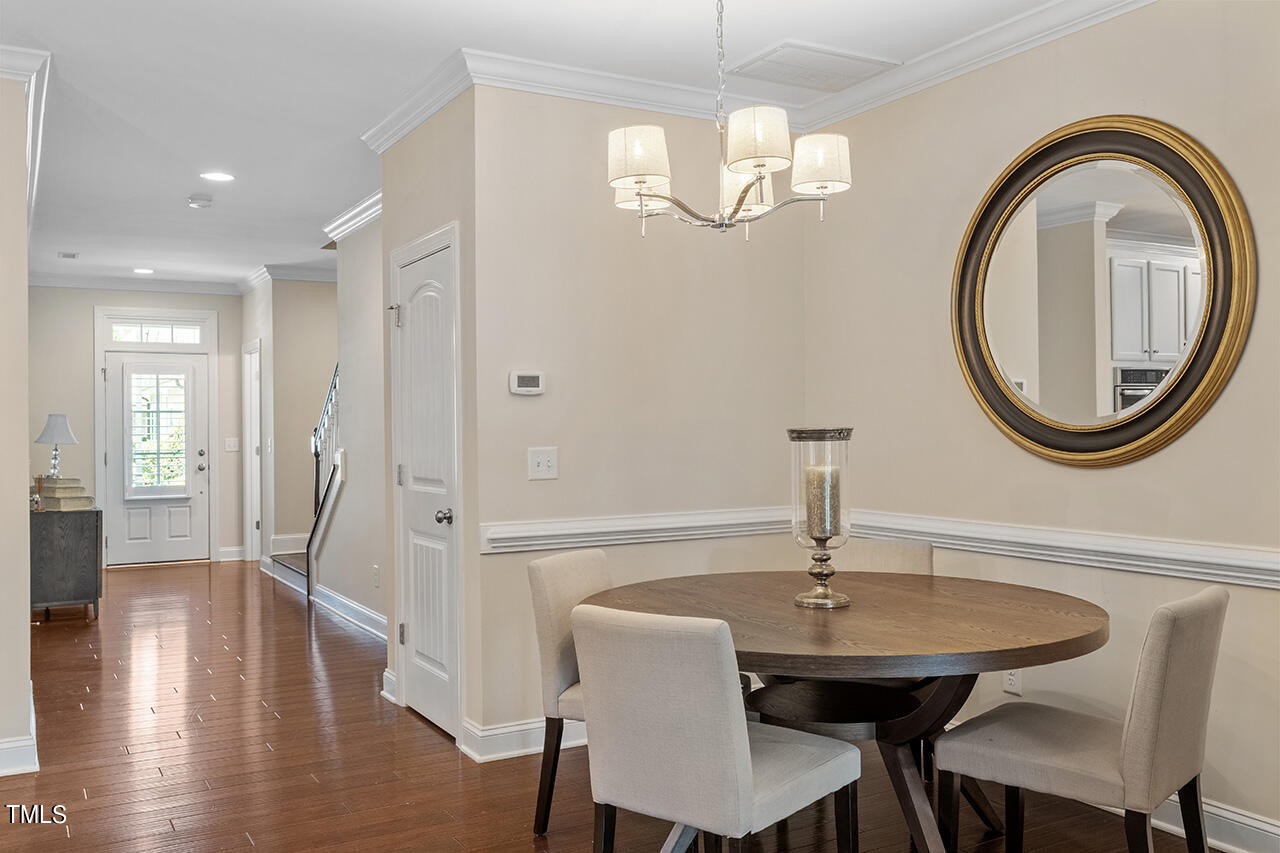 Dining room with a round wooden table, oval mirror, and chandelier beside the entry hall.