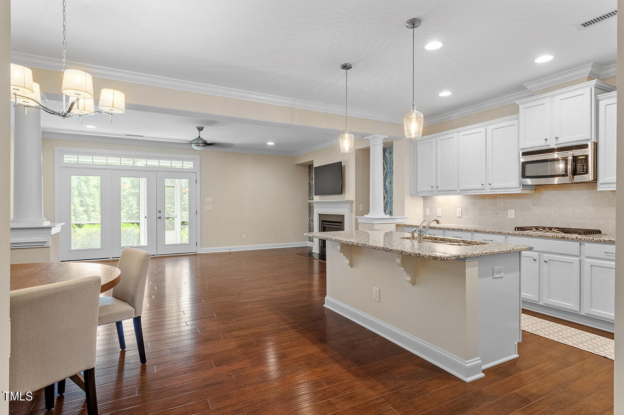 Open-plan kitchen with a granite island, white cabinets, hardwood floors, and glass doors to greenery.