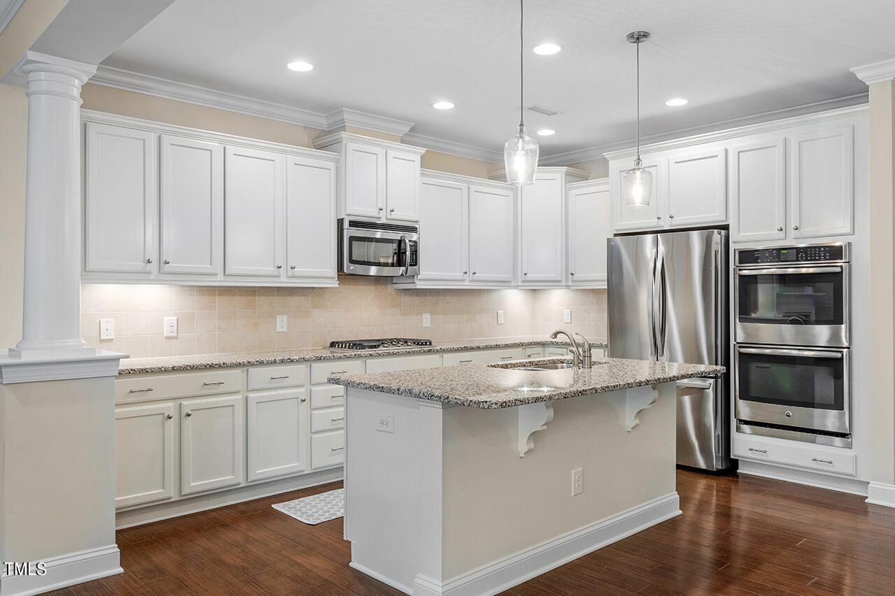 Kitchen with white cabinetry, granite island, stainless steel appliances, and hardwood floors.