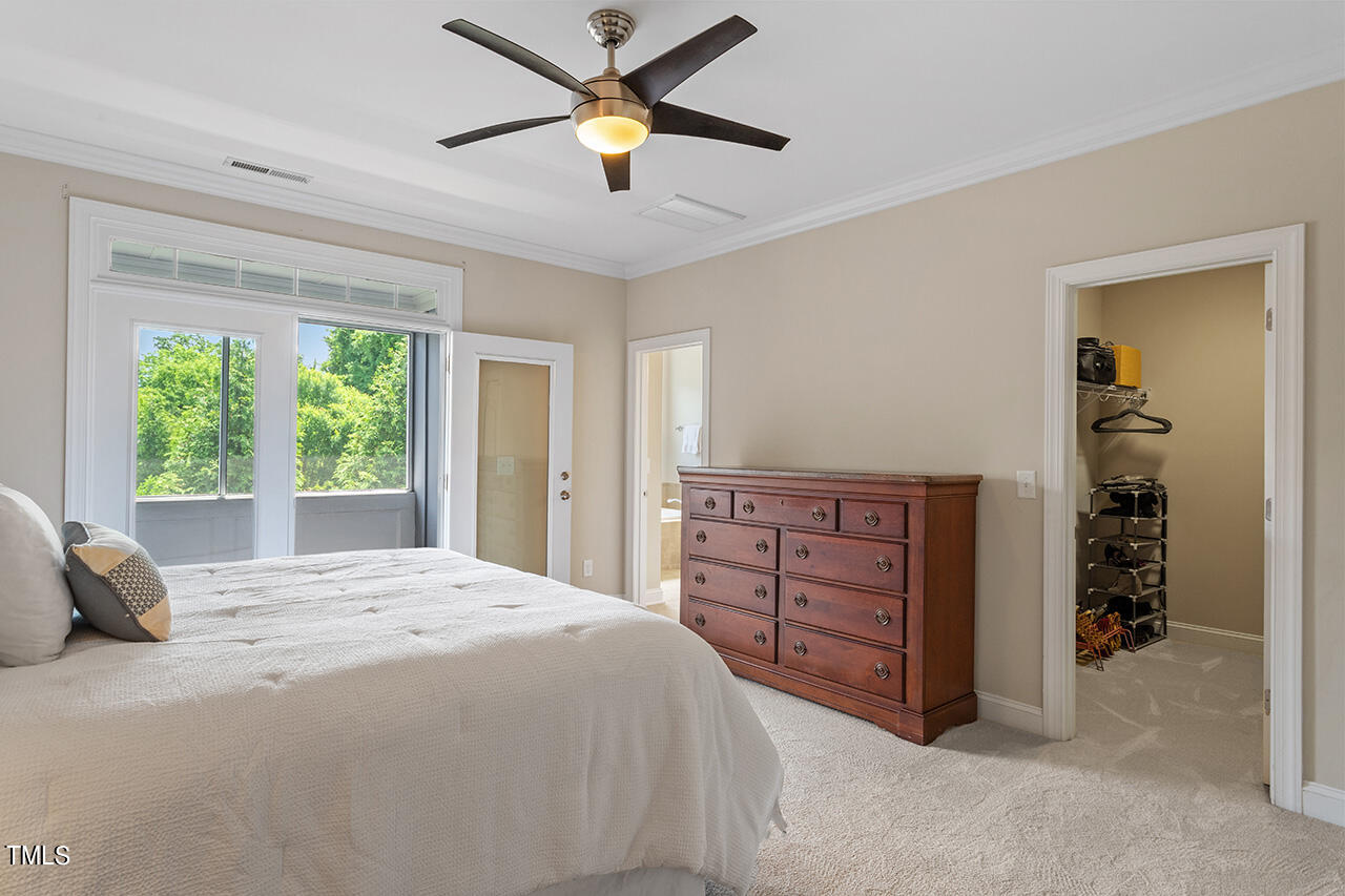 Bedroom with a white bed, dark wood dresser, ceiling fan, and wide window overlooking greenery.
