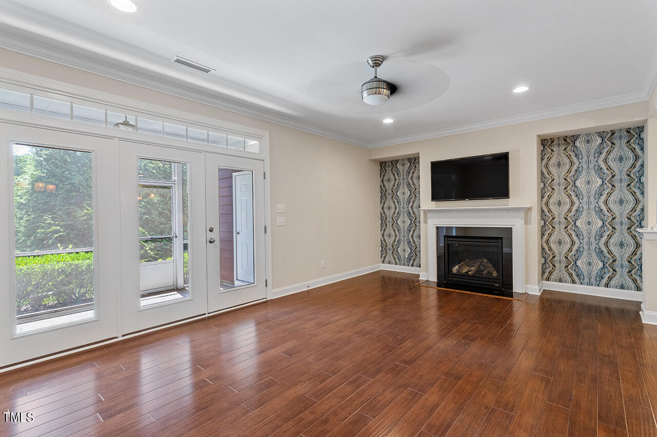 Vacant living room with hardwood floors, a white fireplace, patterned accent walls, and glass doors to a screened porch.