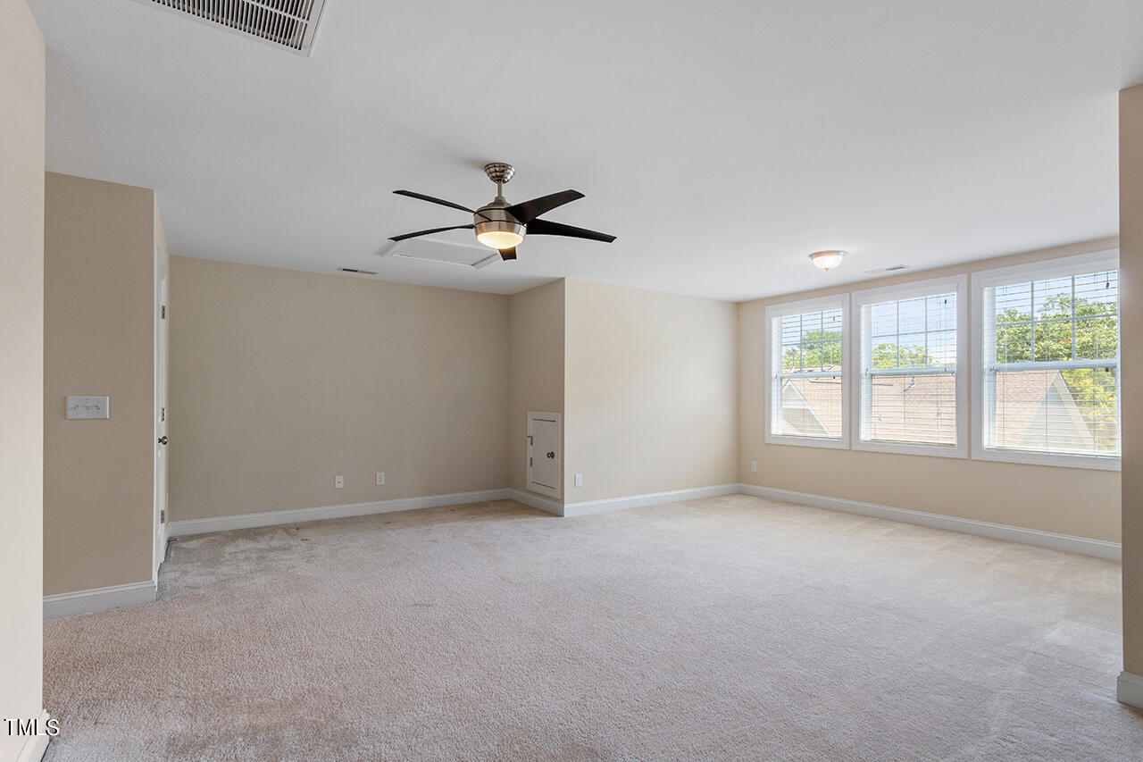 Empty carpeted room with a dark ceiling fan and three windows with white blinds.