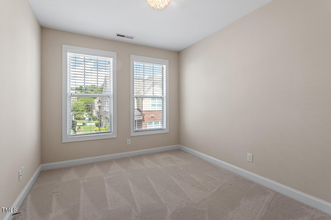 Empty bedroom with beige walls, carpet, and two windows with white blinds.