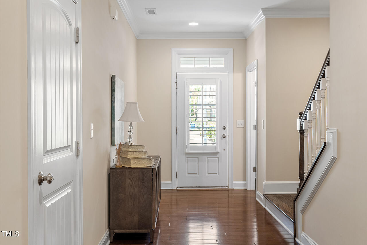 Foyer with hardwood floors, a shuttered glass-panel front door, console table, and staircase.