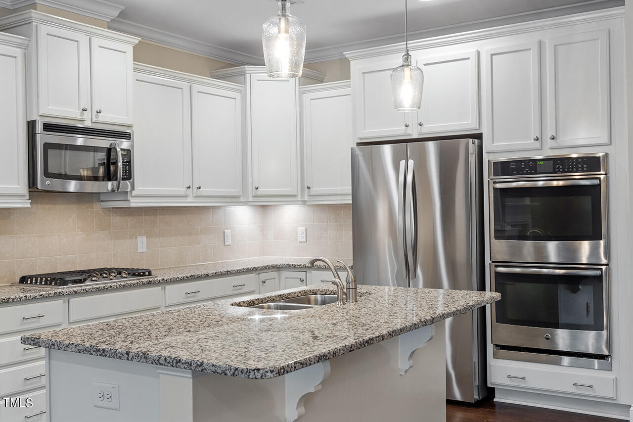 Kitchen with a granite island, white cabinets, stainless steel appliances, and double wall ovens.