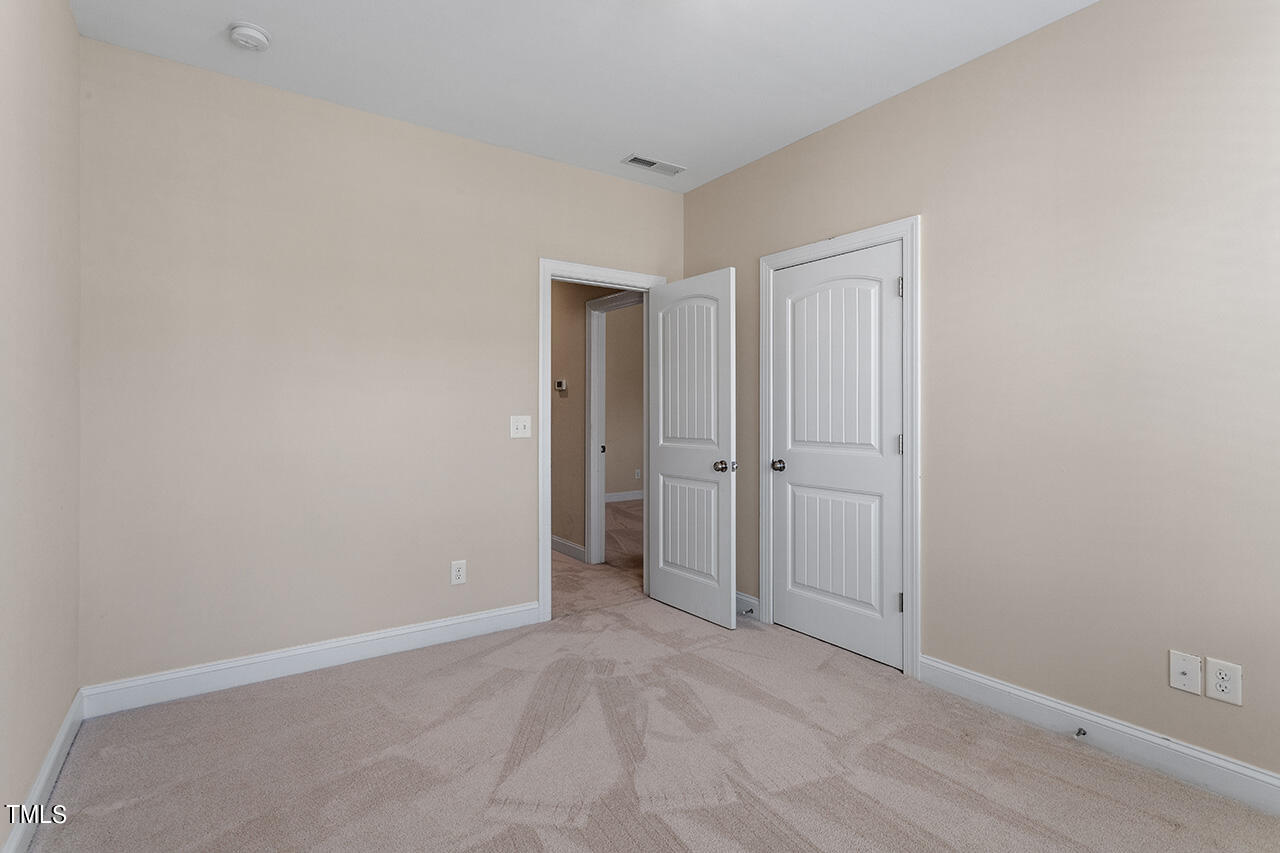 Empty bedroom with light carpet and two white paneled doors.
