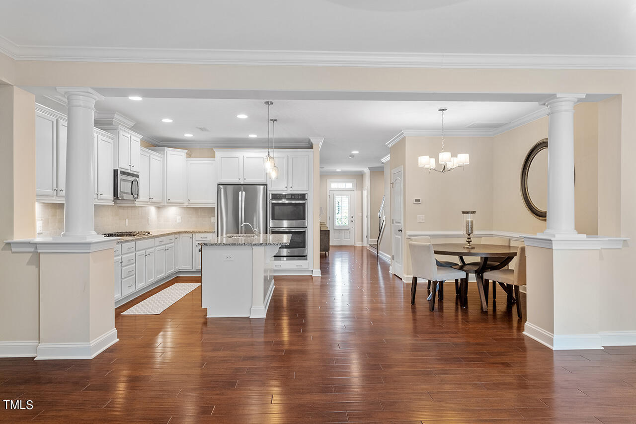 Open-plan kitchen and dining area with white cabinets, stainless steel appliances, and a granite island.