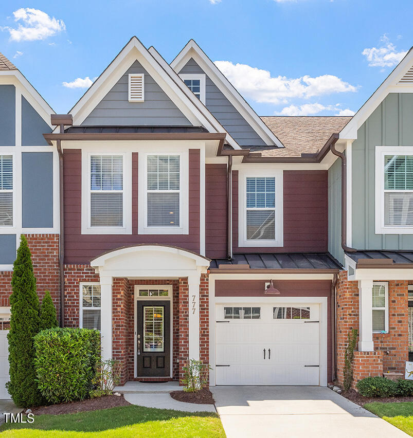 Two-story townhouse with burgundy siding, brick accents, steep gables, and a white garage door.