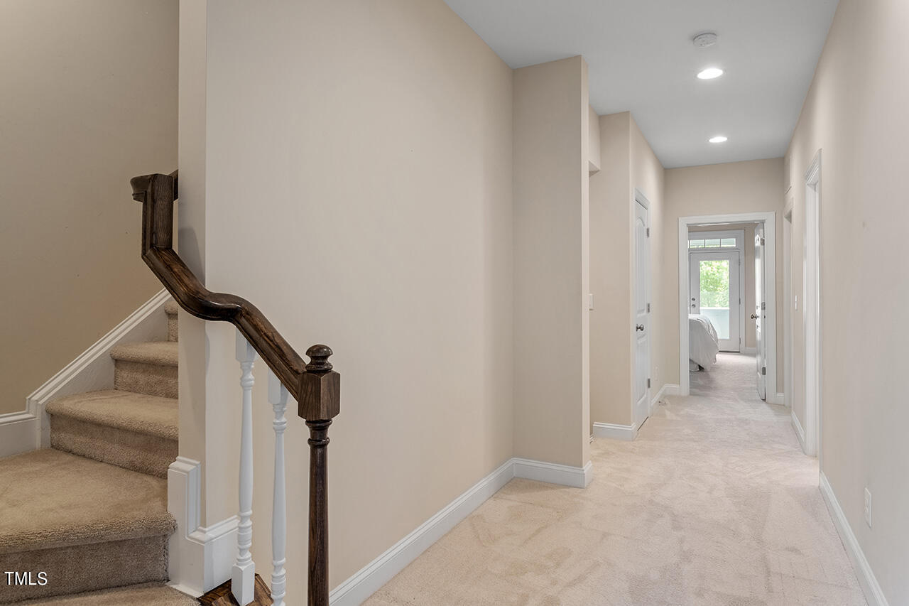 Carpeted hallway beside a staircase with a dark wood handrail and a bedroom at the far end.