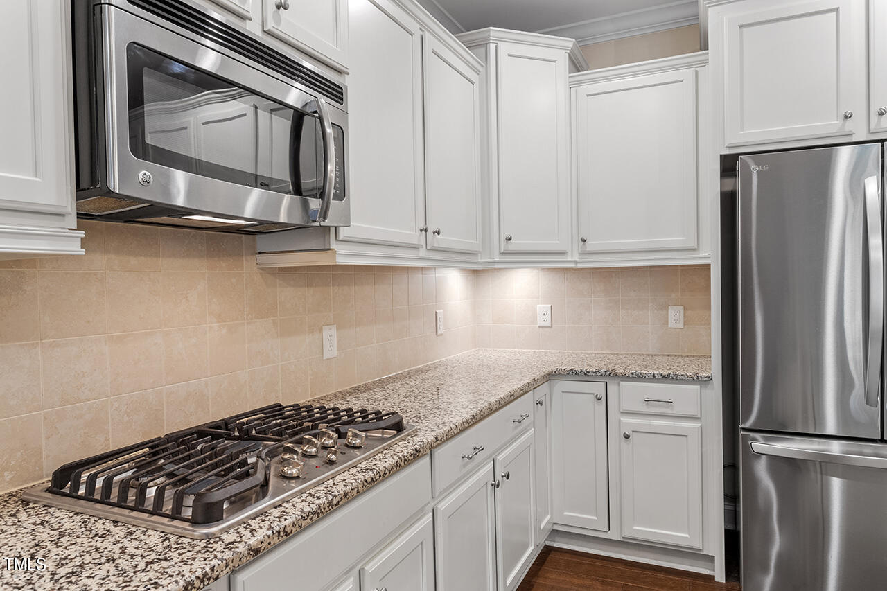 Kitchen with white cabinets, granite counters, gas cooktop, and stainless steel appliances.