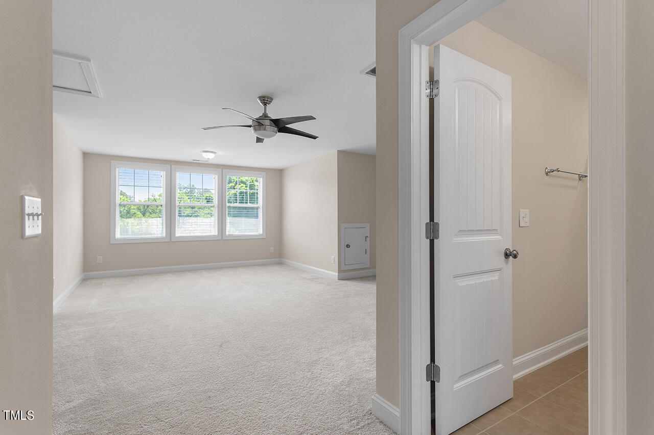 Carpeted bedroom with three windows and a ceiling fan, viewed beside an open bathroom door.