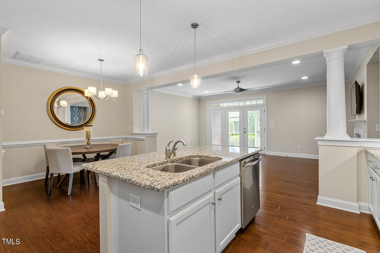 Open-plan kitchen with a granite-topped island, double sink, stainless dishwasher, and adjoining dining area.