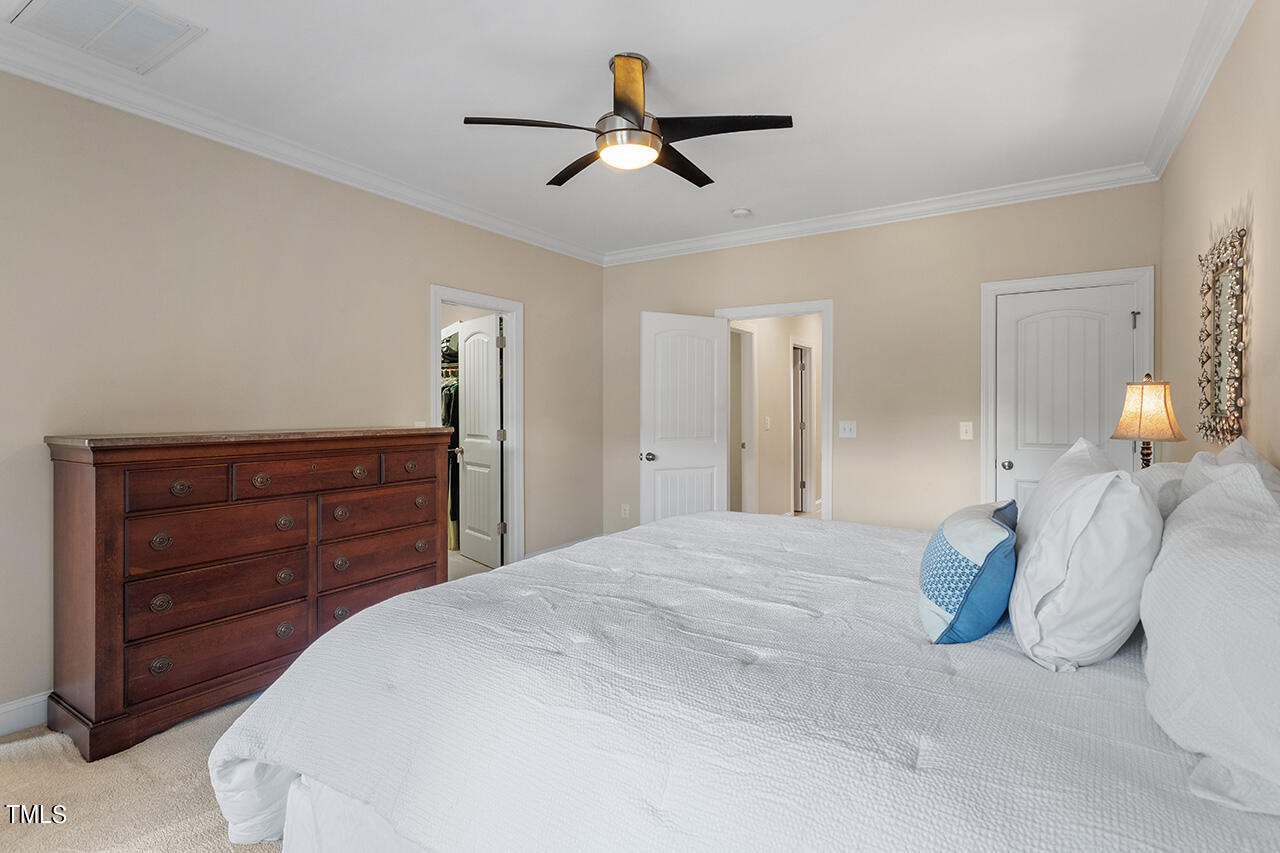 Furnished bedroom with a white bed, dark wood dresser, and ceiling fan.