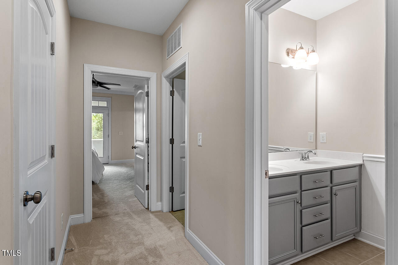 Carpeted hallway beside a bathroom vanity with gray cabinetry, leading toward a bedroom.