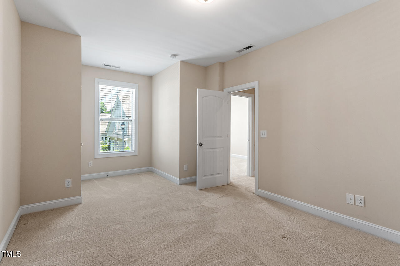 Empty carpeted bedroom with a window and an open door to another room.