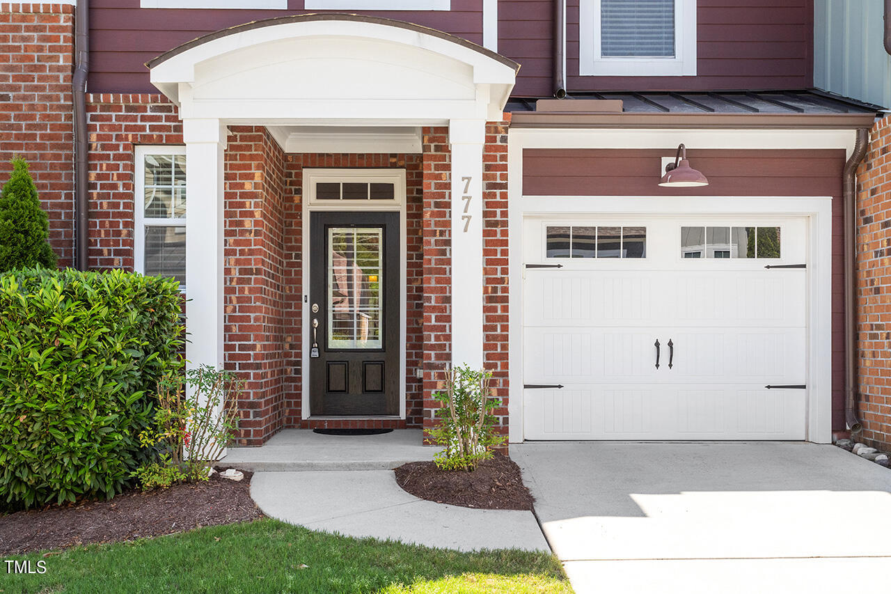 Brick home entrance with a white covered porch, dark front door, and adjoining garage.