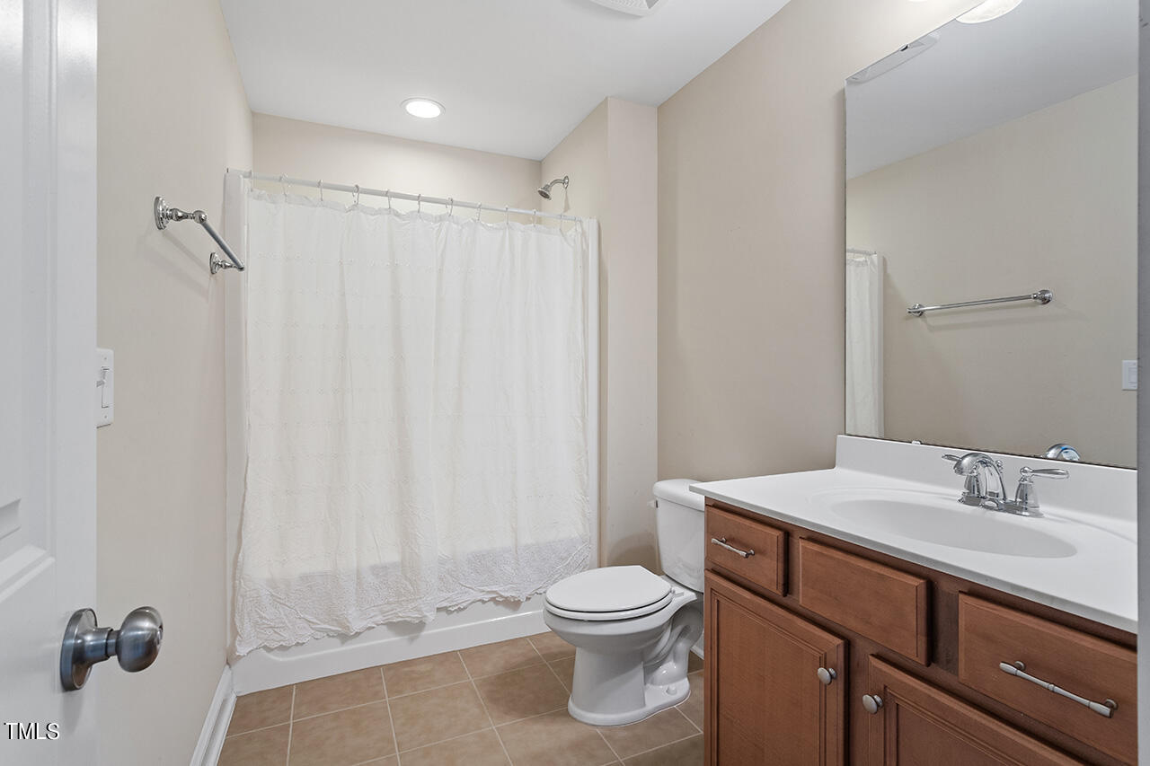 Bathroom with a curtained tub and shower, toilet, and wood vanity beneath a large mirror.