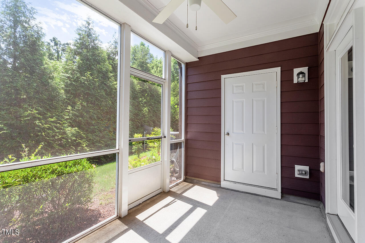 Enclosed porch with large windows overlooking trees and a white door against dark siding.
