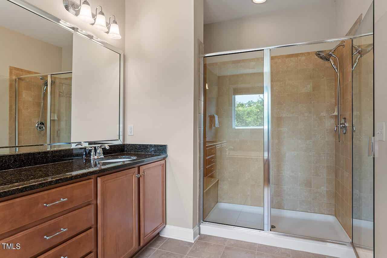 Bathroom with a dark stone vanity and a glass-enclosed beige-tile shower.