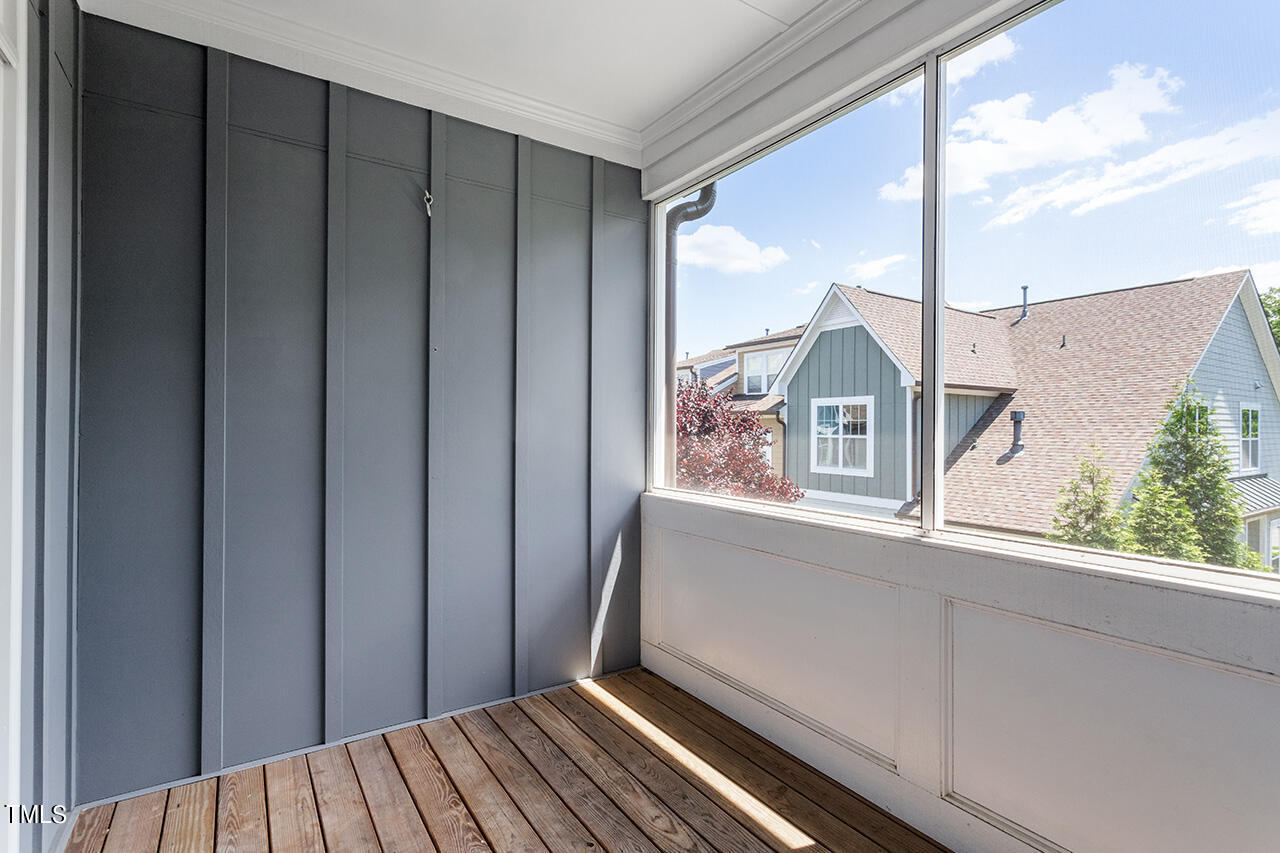 Enclosed porch with gray paneled walls, wood flooring, and large windows overlooking a neighboring home.