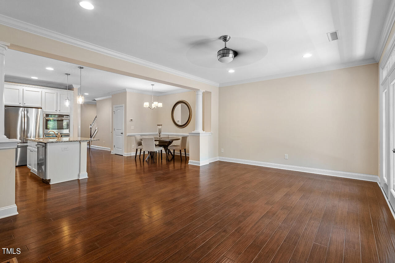 Open-plan living area with hardwood floors, white kitchen, and dining table beneath a chandelier.