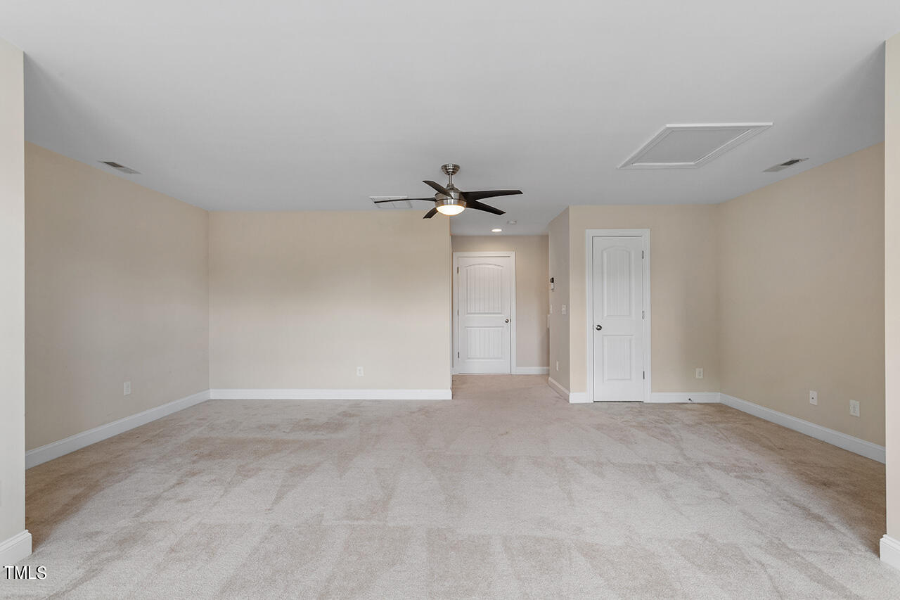 Empty carpeted room with beige walls, a dark ceiling fan, and two white paneled doors.