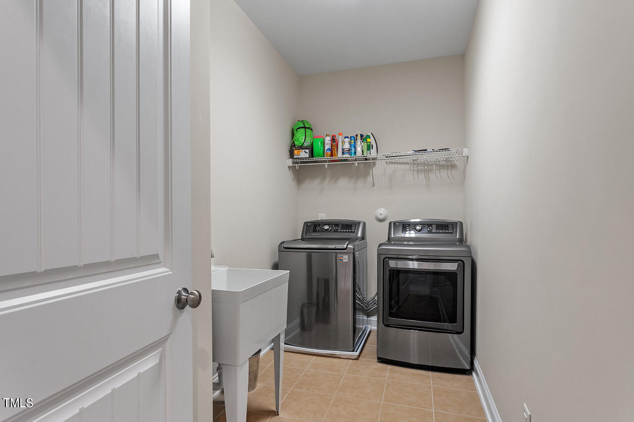 Laundry room with stainless steel washer and dryer, utility sink, and shelf of cleaning supplies.