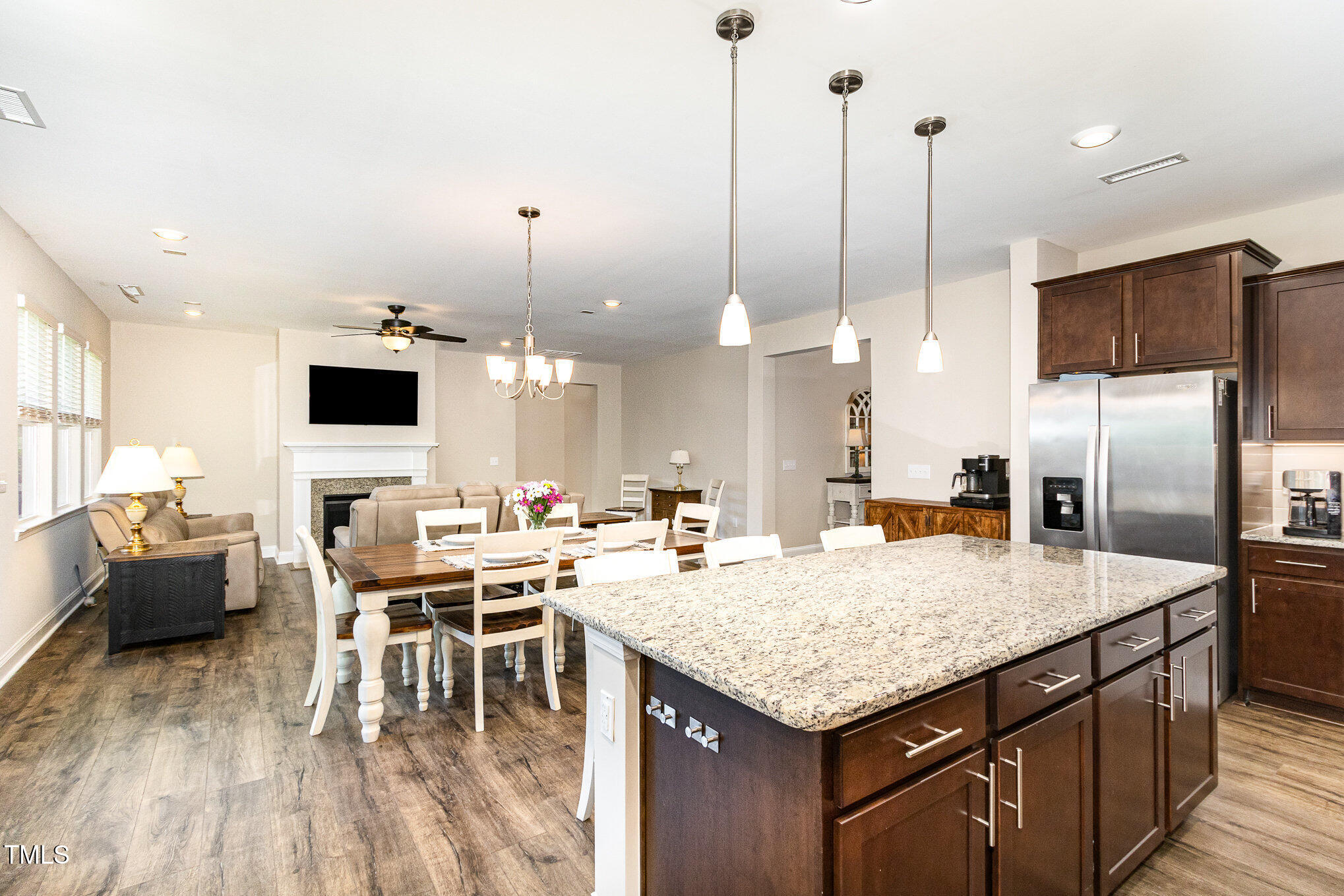 Open-plan kitchen and living area with a granite island, dark cabinets, dining table, and fireplace.