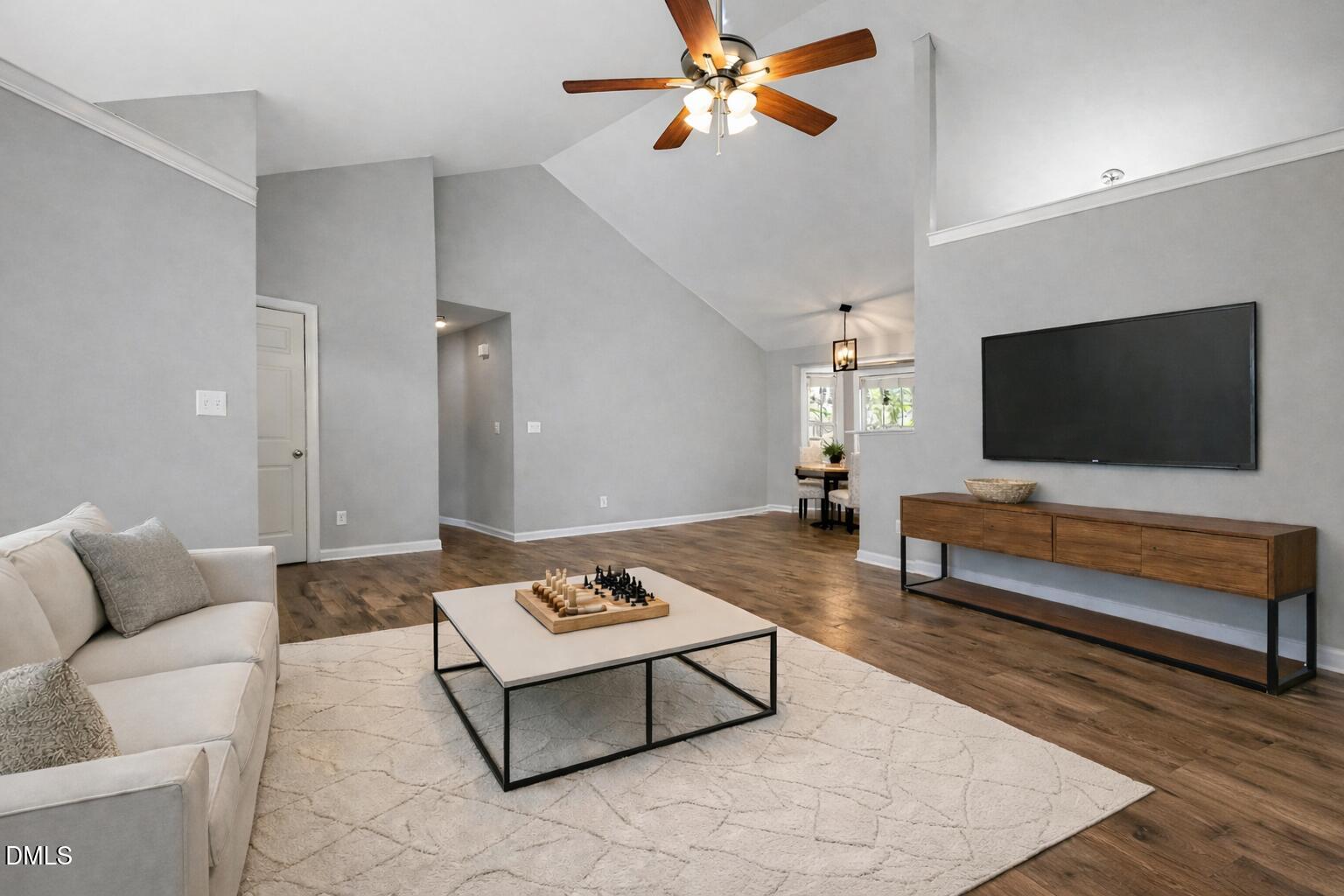 Living room with vaulted ceiling, wood floors, and a wall-mounted TV above a wood console.