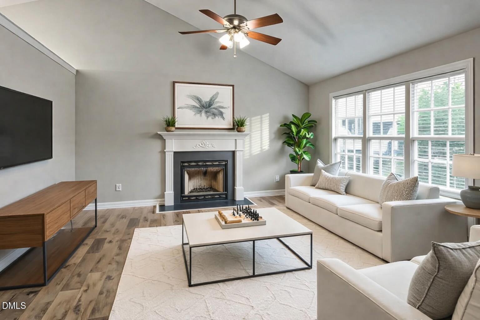 Living room with a fireplace, vaulted ceiling, large windows, and cream sofas.