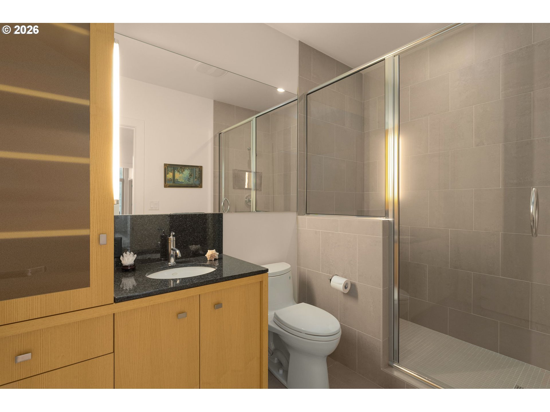 Bathroom with a glass-enclosed tiled shower and light wood vanity.