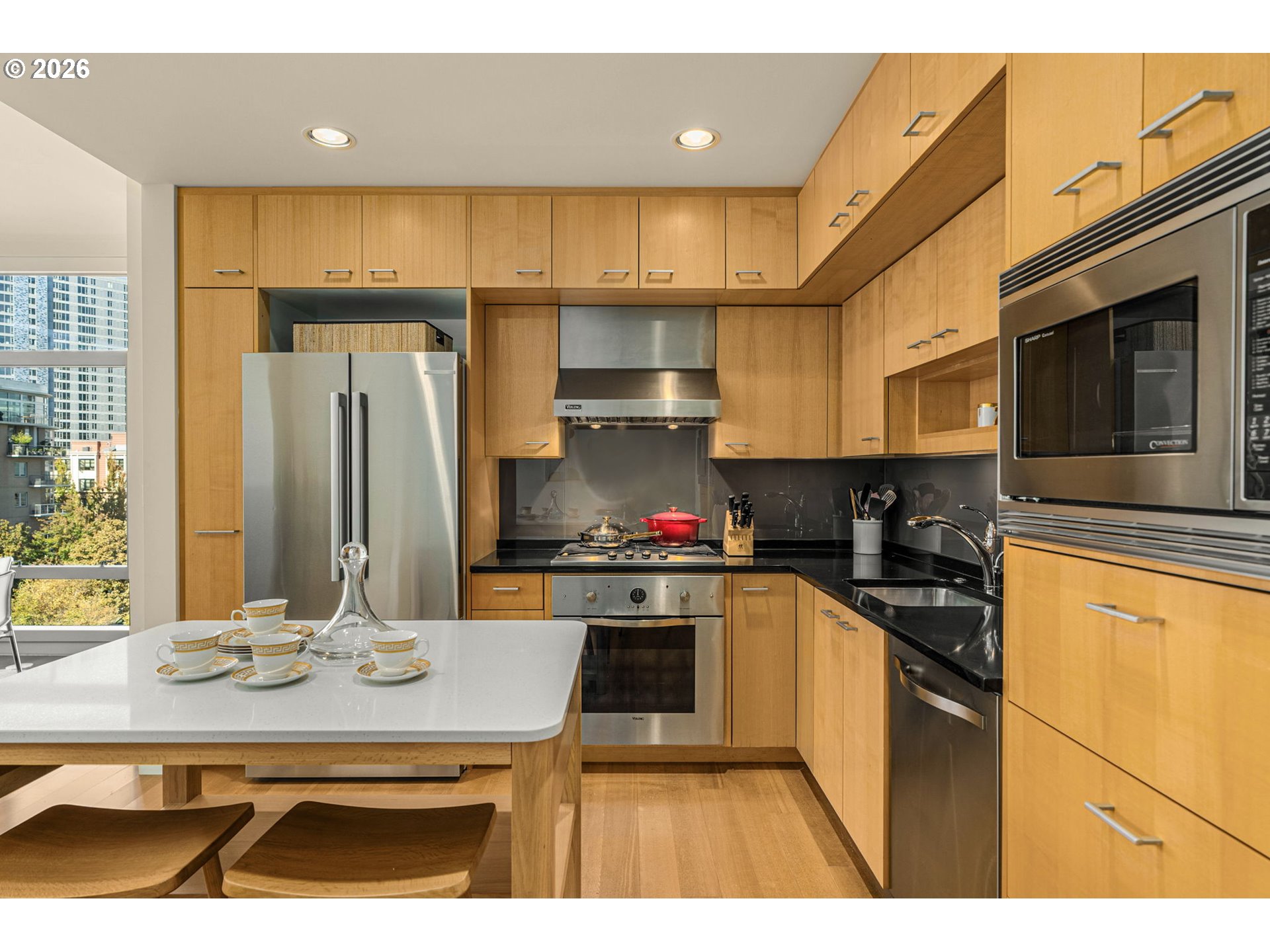 Condominium kitchen with warm wood cabinets, stainless-steel appliances, and a white island set with teacups.