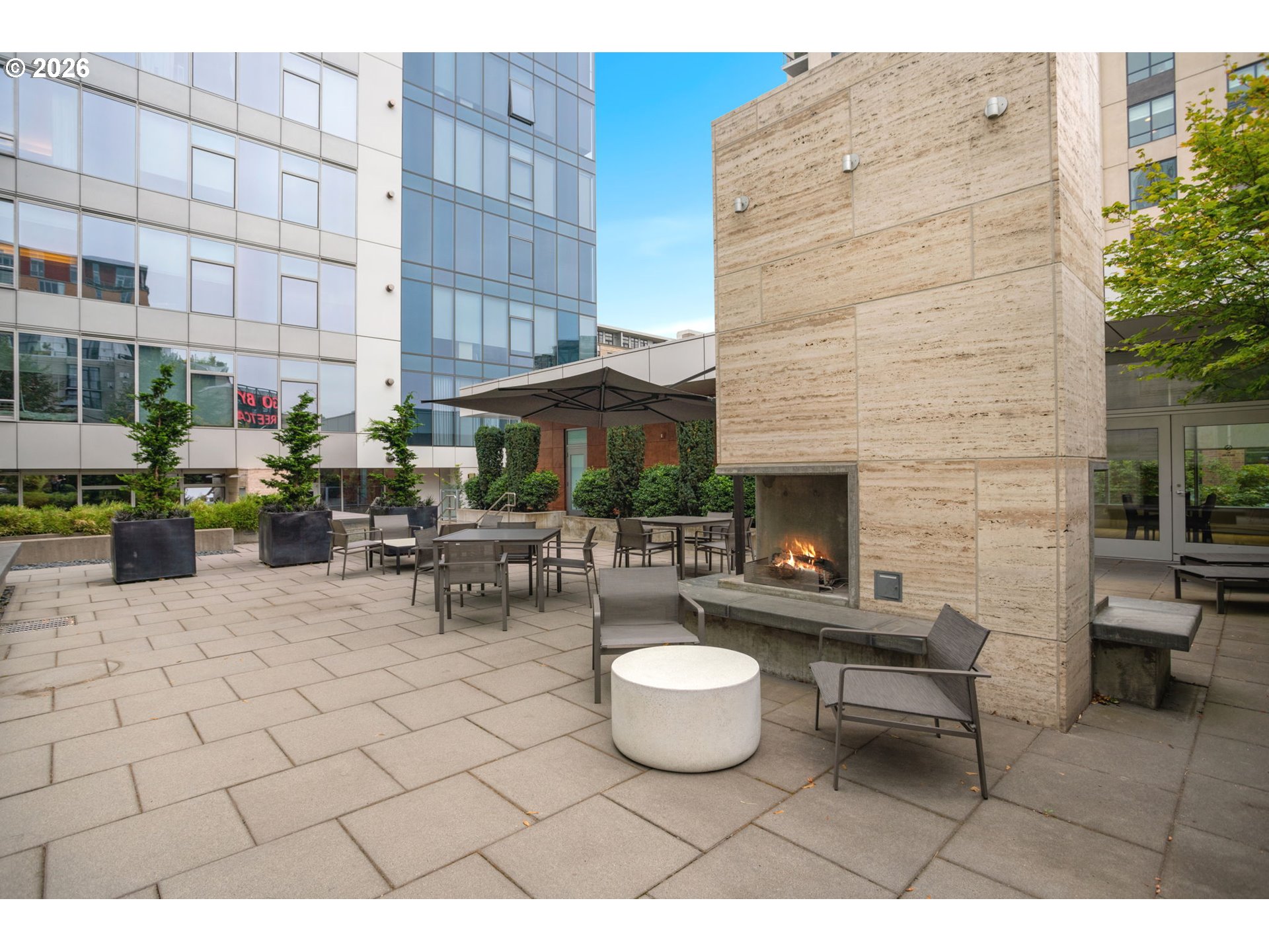 Apartment courtyard terrace with lounge seating, planters, and a large stone fireplace.