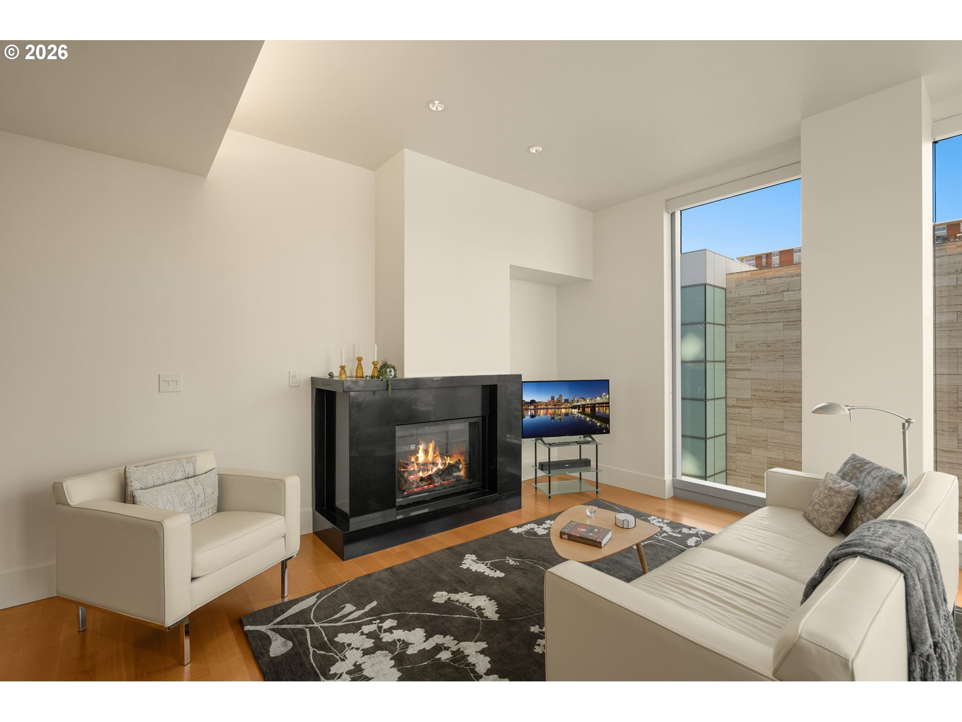 Condo living room with a black fireplace, cream sofas, and a large window.