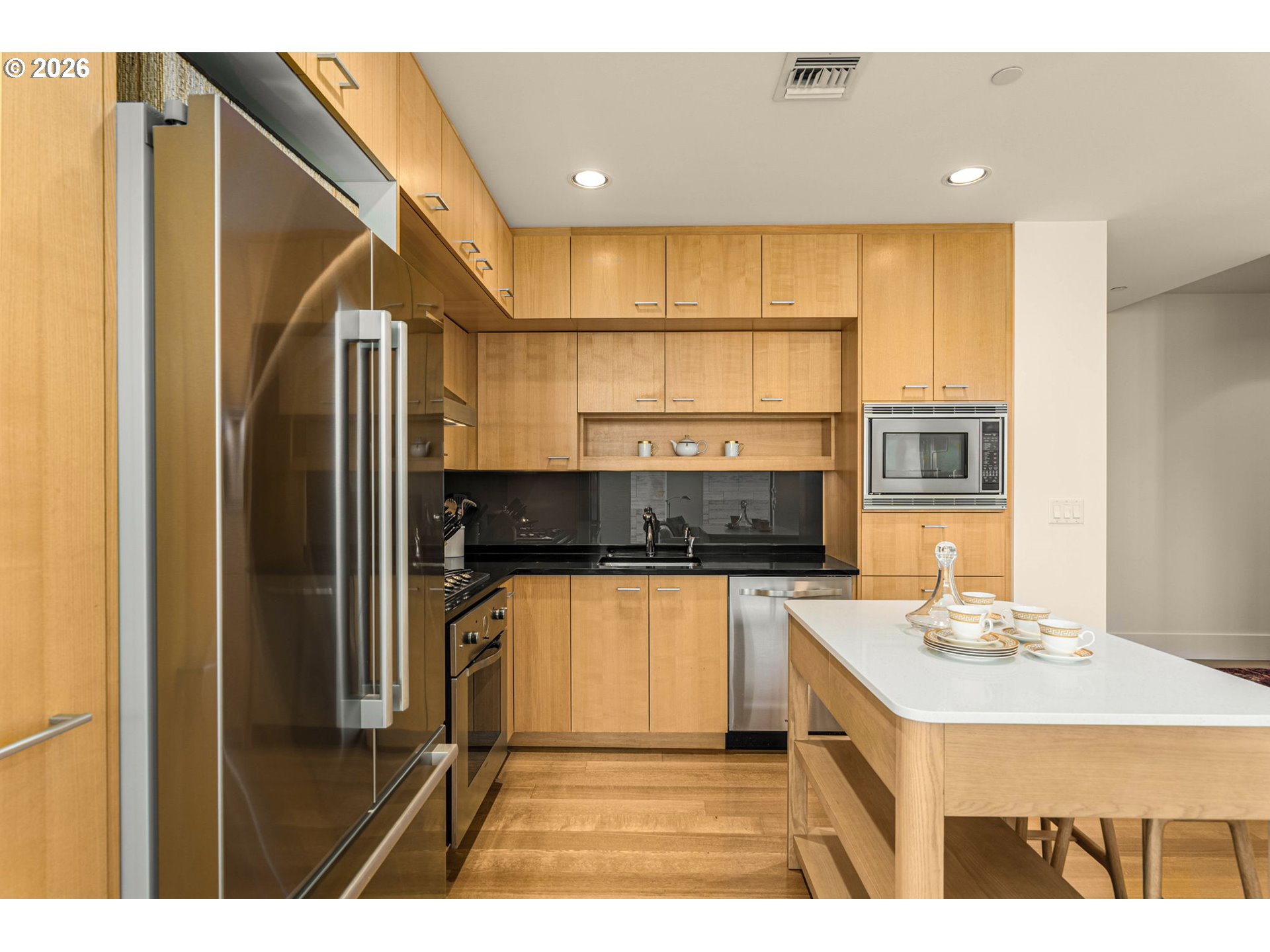 Modern kitchen with wood cabinetry, stainless steel appliances, and a white island set with dishes.