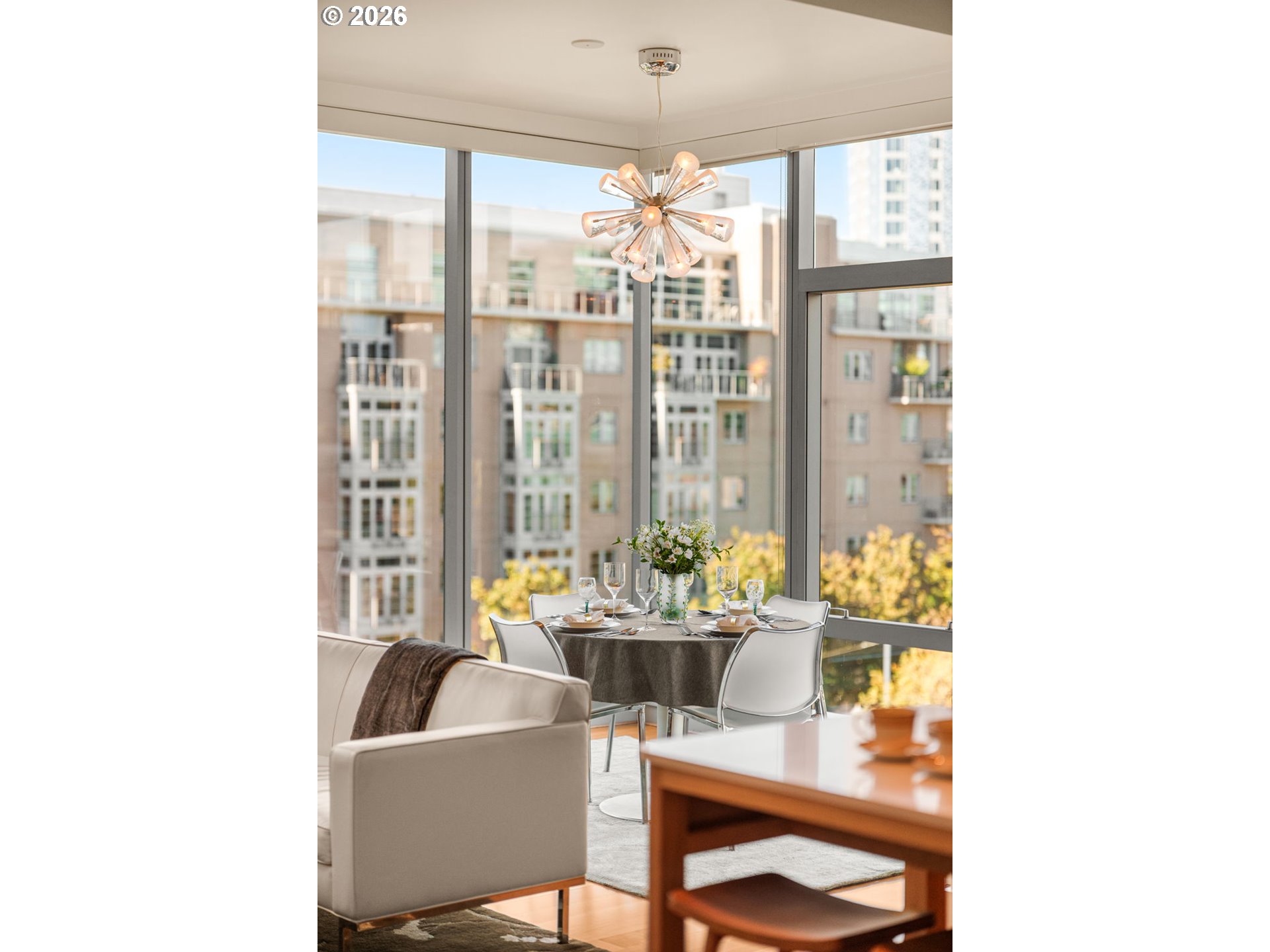 Staged condo living and dining area with floor-to-ceiling windows overlooking neighboring buildings.