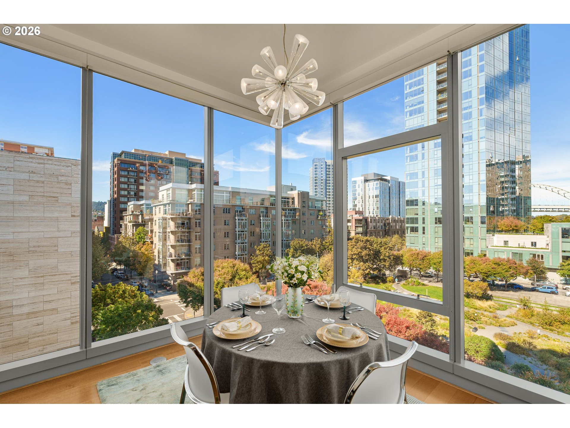Dining area with a set table and floor-to-ceiling windows overlooking downtown buildings.