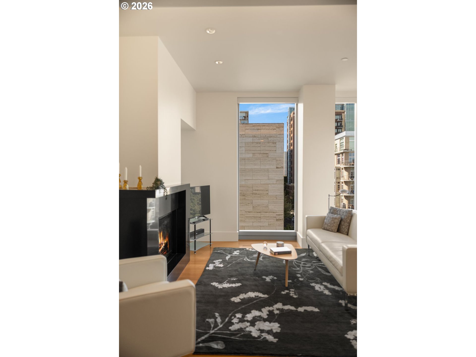 Condominium living room with a black fireplace, white sofas, and tall windows overlooking city buildings.