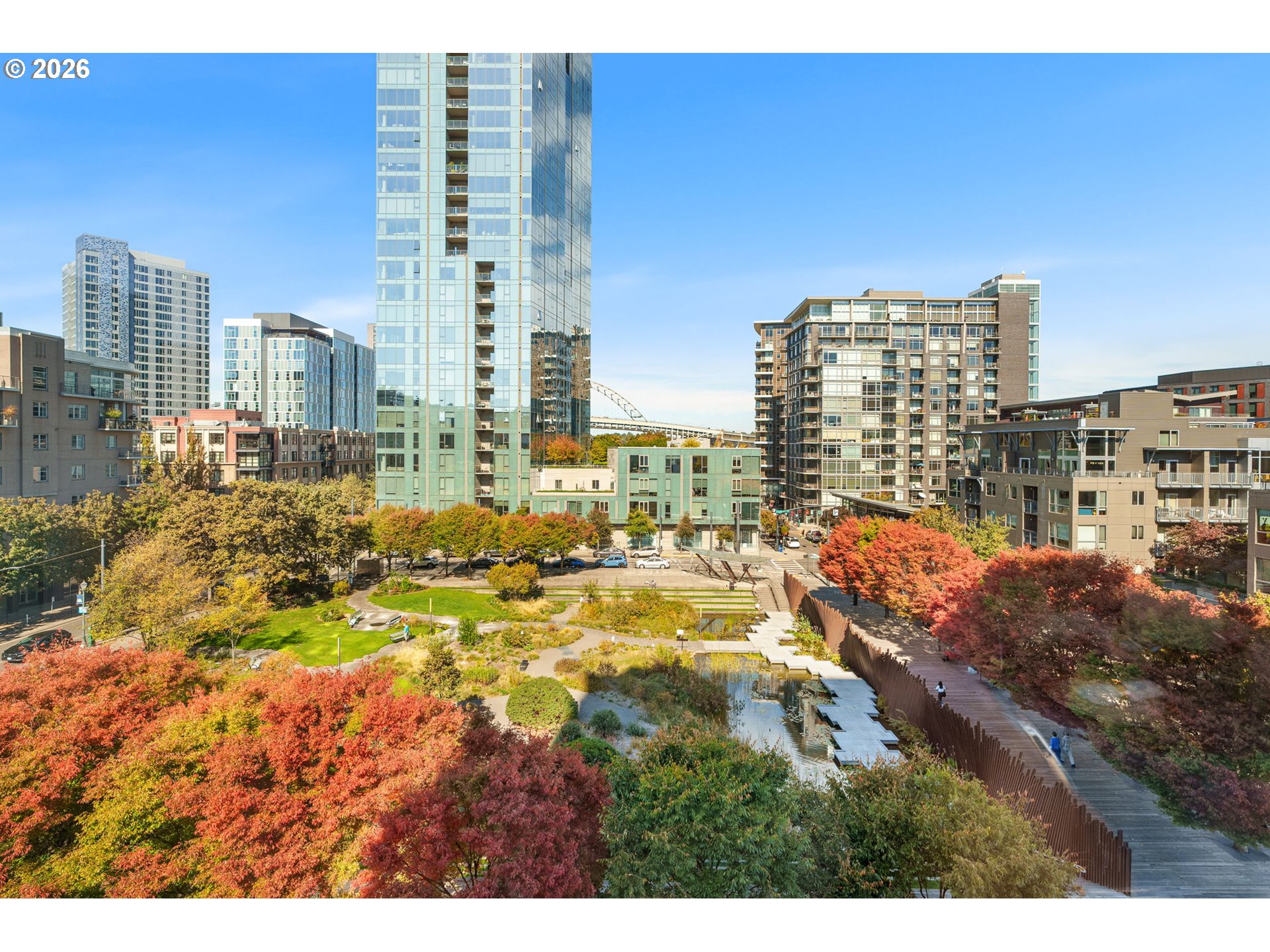 Elevated view over an autumn park and reflecting pool, framed by apartment towers.