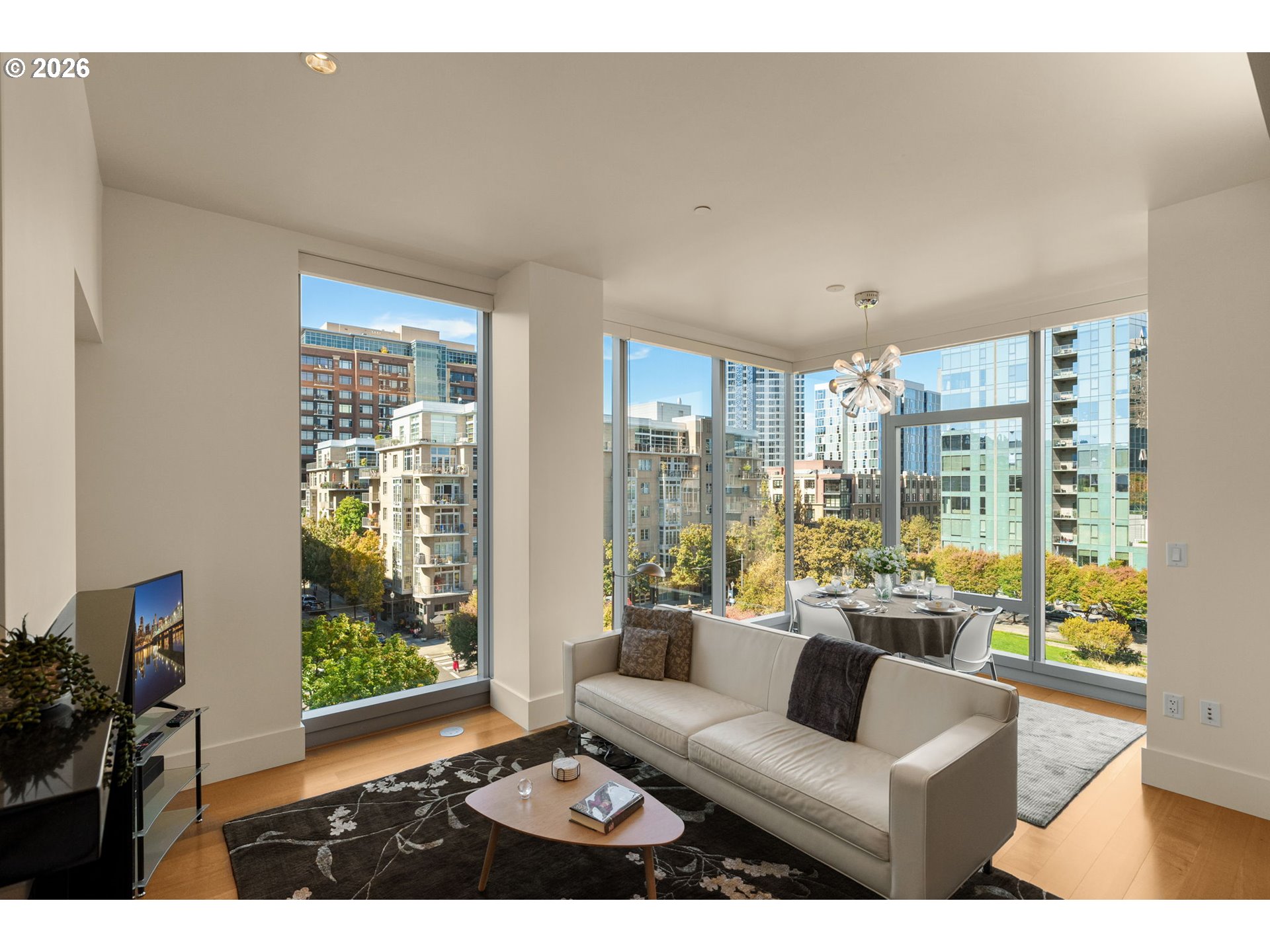 Condo living room with floor-to-ceiling windows overlooking downtown buildings and autumn trees.