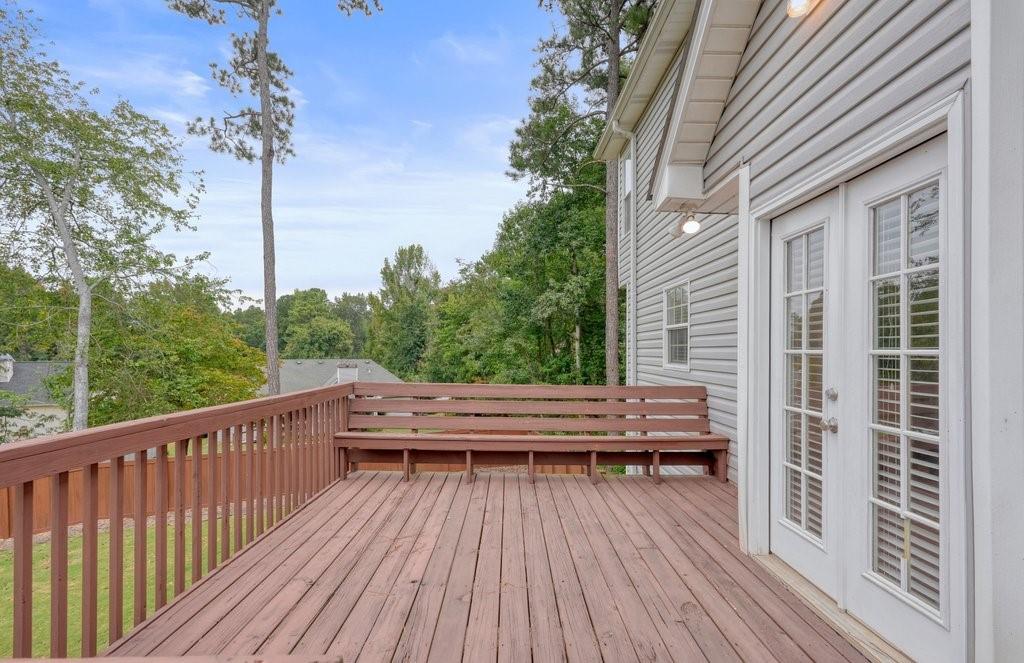 Raised wooden deck with a built-in bench, white French doors, and leafy trees beyond the railing.