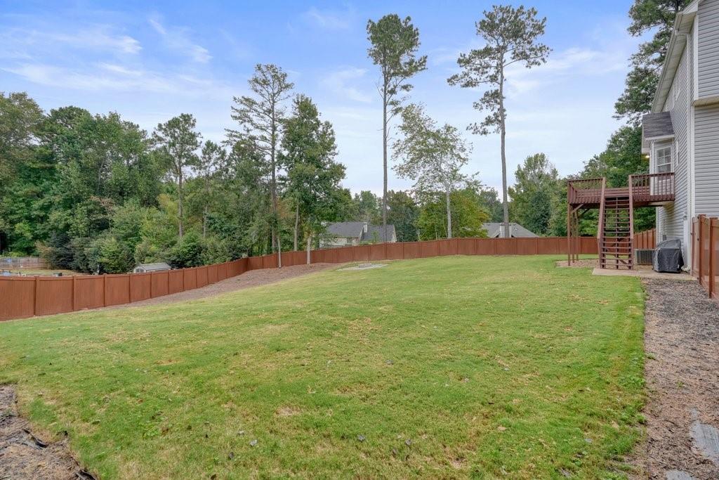 Grassy backyard enclosed by a wooden privacy fence, with mature trees and a raised deck beside the house.