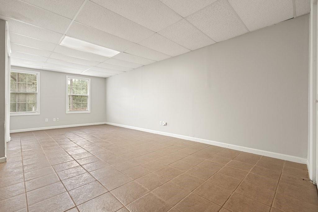 Empty room with tan tile flooring, a suspended ceiling, and two windows.