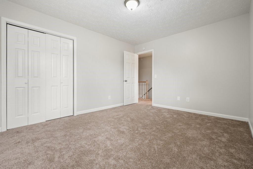 Empty bedroom with beige carpet, a double-door closet, and an open doorway to the stairs.