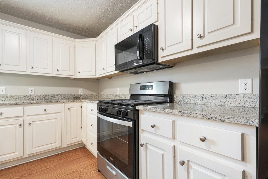 Kitchen with white cabinets, granite counters, and a black range beneath a microwave.