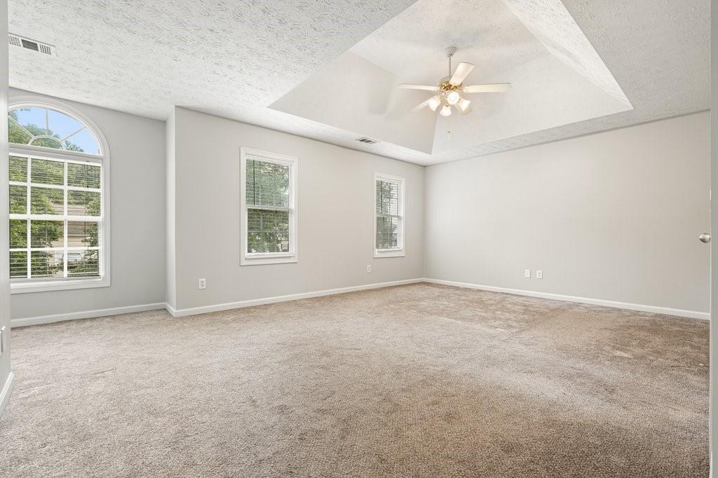 Empty carpeted bedroom with an arched window and ceiling fan beneath a vaulted ceiling.